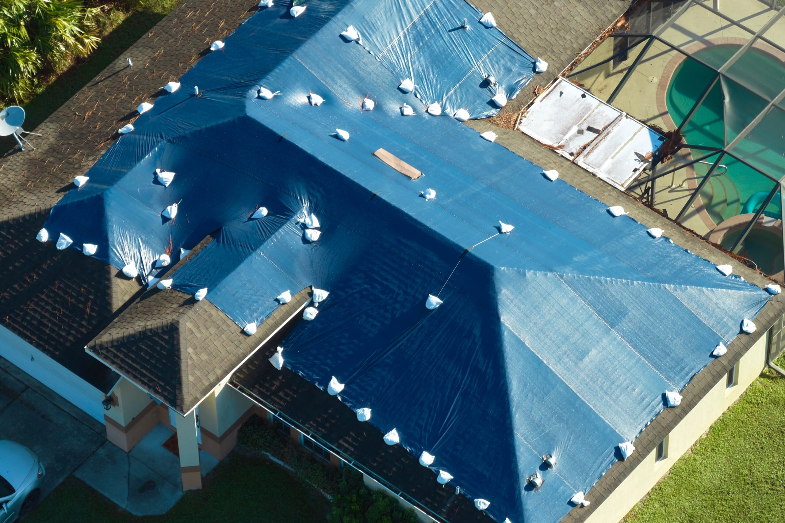 Aerial view of a residential roof covered with blue protective tarp secured with white fasteners in Elyria, OH