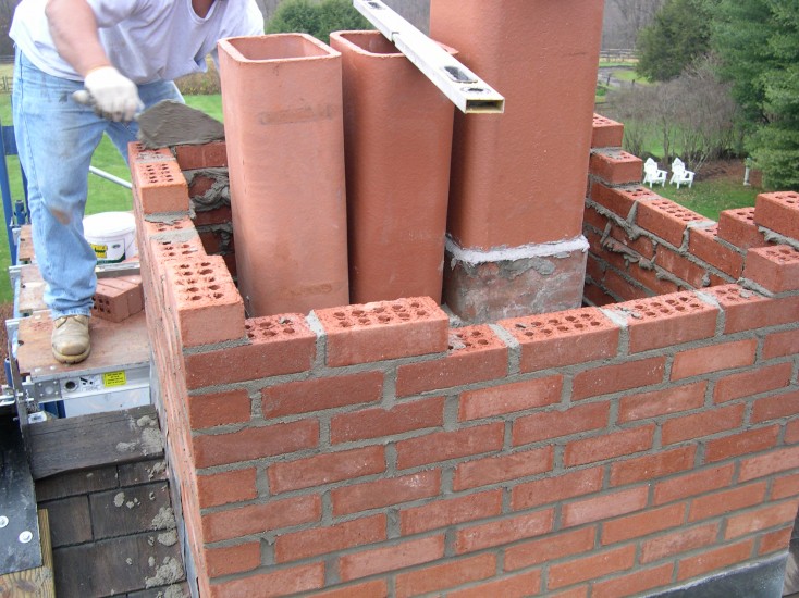 Bricklayer constructs a residential chimney using red bricks and terracotta flue pipes in Medina, OH