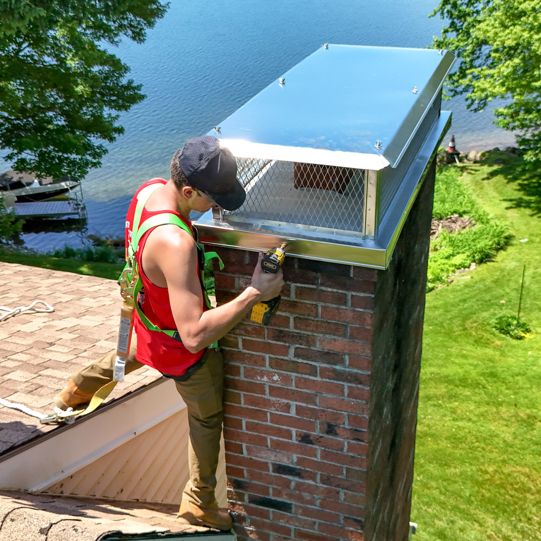 Worker installing custom chimney cap on brick chimney overlooking lake