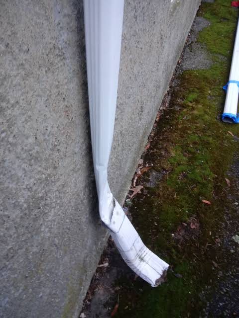 Crushed white downspout against concrete wall requiring replacement