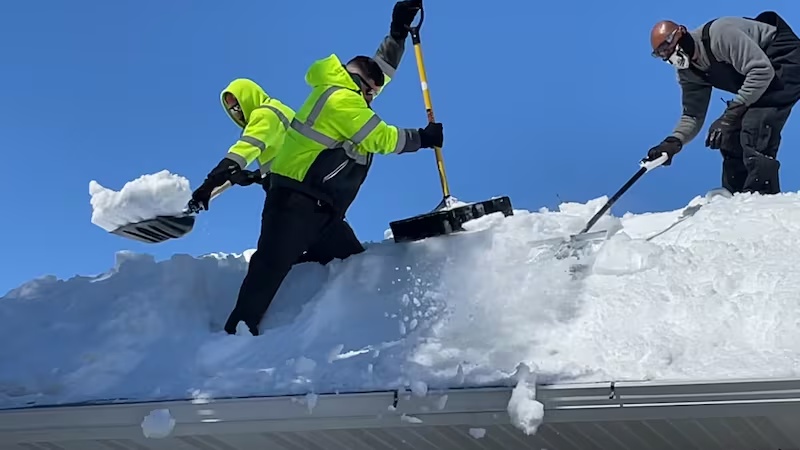 Professional workers safely remove heavy ice buildup from a residential roof on a clear winter day in Kent, OH