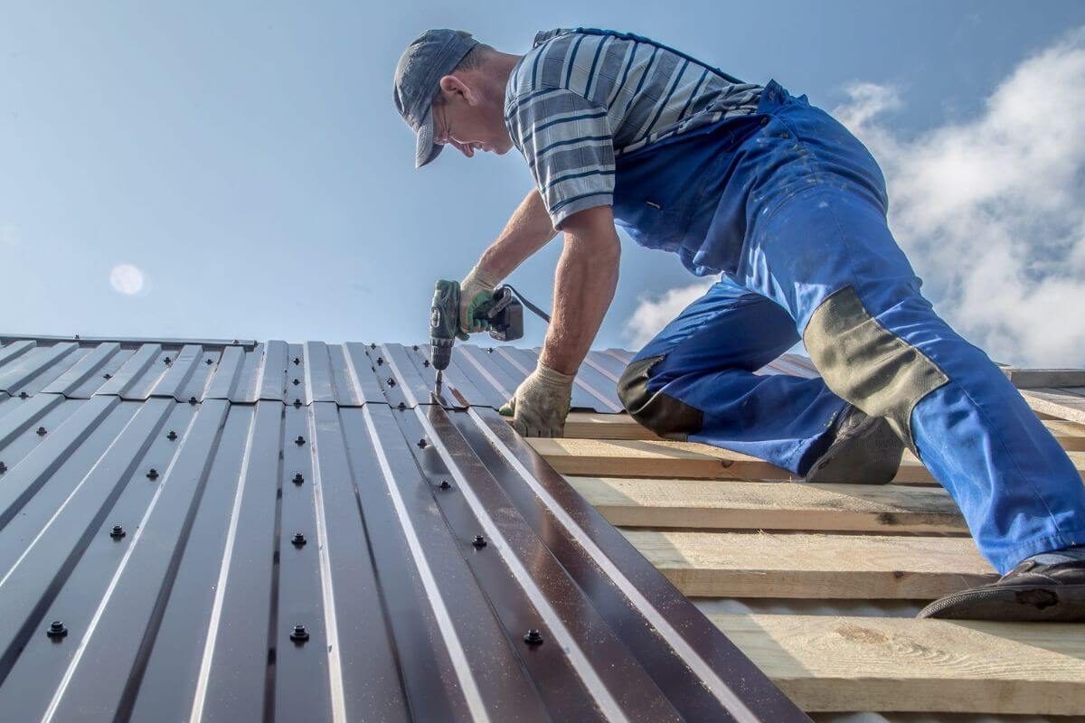 Worker installing standing seam metal roof panels on wooden frame