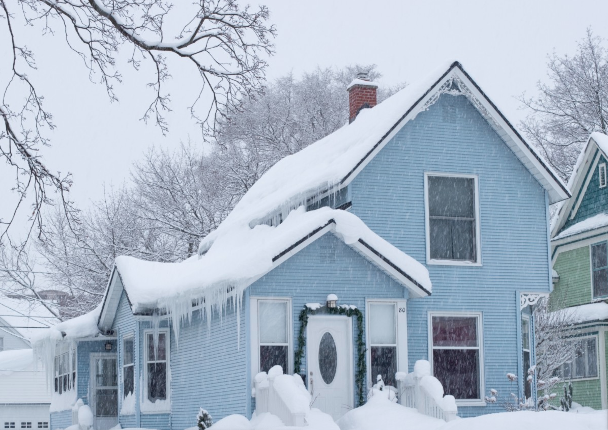 A blue residential home heavily laden with snow and dangerous icicles forming along the roofline in Kent, OH